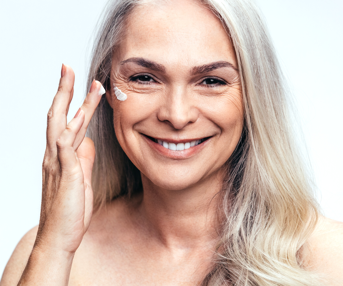 A middle-aged woman applies anti-aging skin care to the fine lines around her eyes.