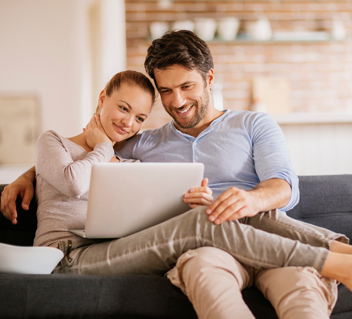 A man and a woman sit on the couch looking at a laptop together.