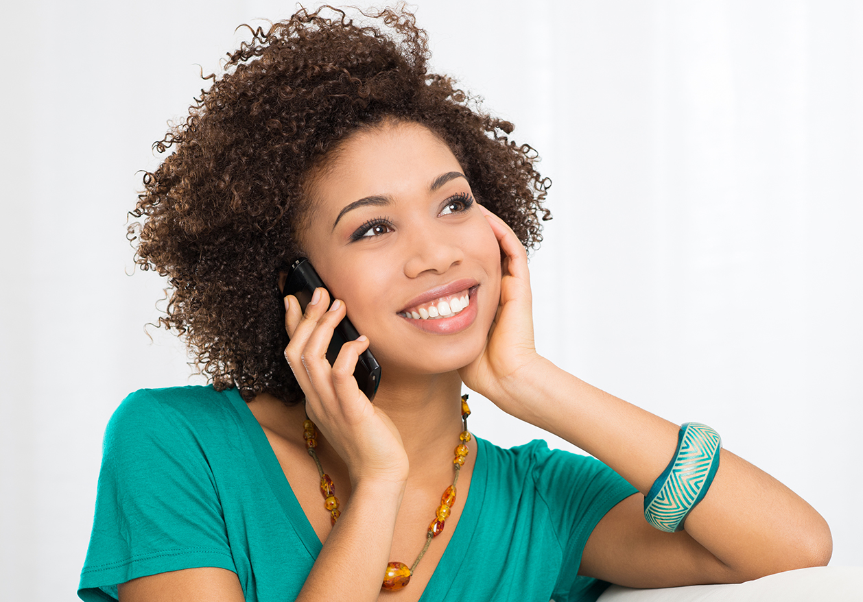 A black woman smiles as she talks on the phone to book an IV therapy appointment.