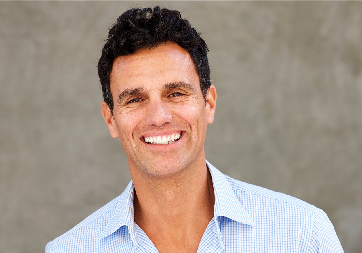 A confident man with dark hair smiles at the camera.