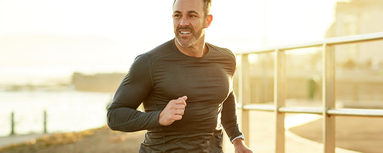 A fit man runs around a lake smiling.