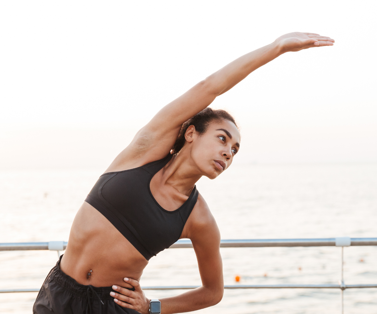 A black woman in athletic wear stretches during her outdoor exercise to show the benefit of anabolic androgenic therapy for joints.