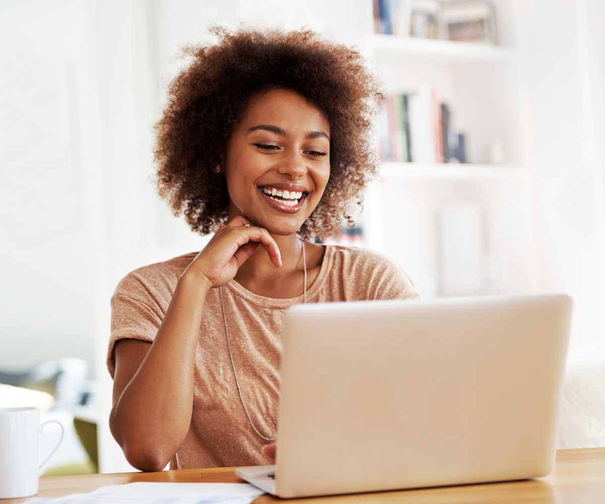 A Black woman smiles as she looks at her laptop.