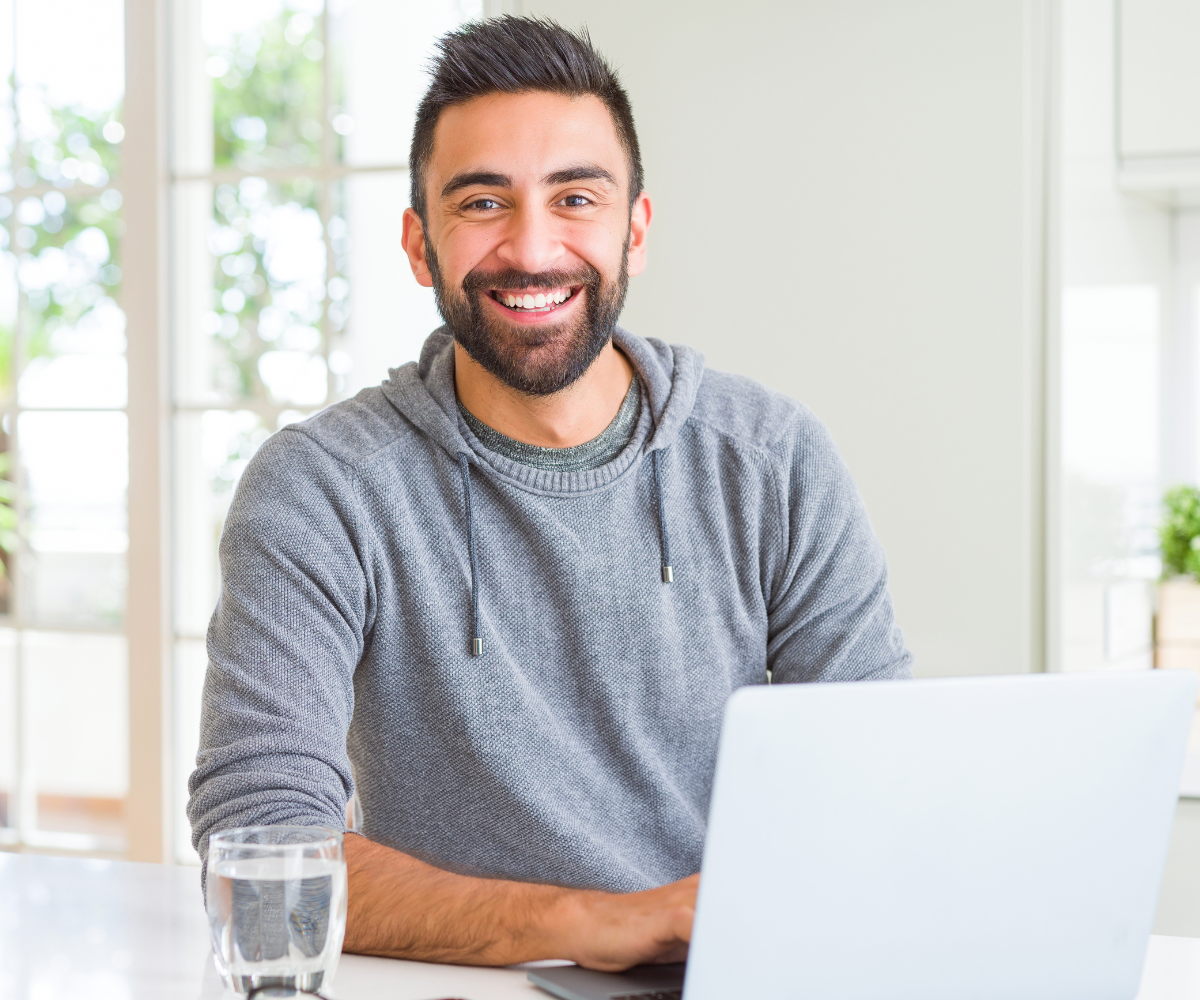 A man with dark hair and a beard smiles as he uses his laptop to look up the complete guide to TRT.