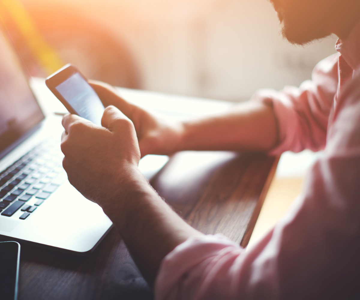 A man sits in front of a keyboard and holds his smart phone in his hand as he researches Defy Medical's advice only consults.