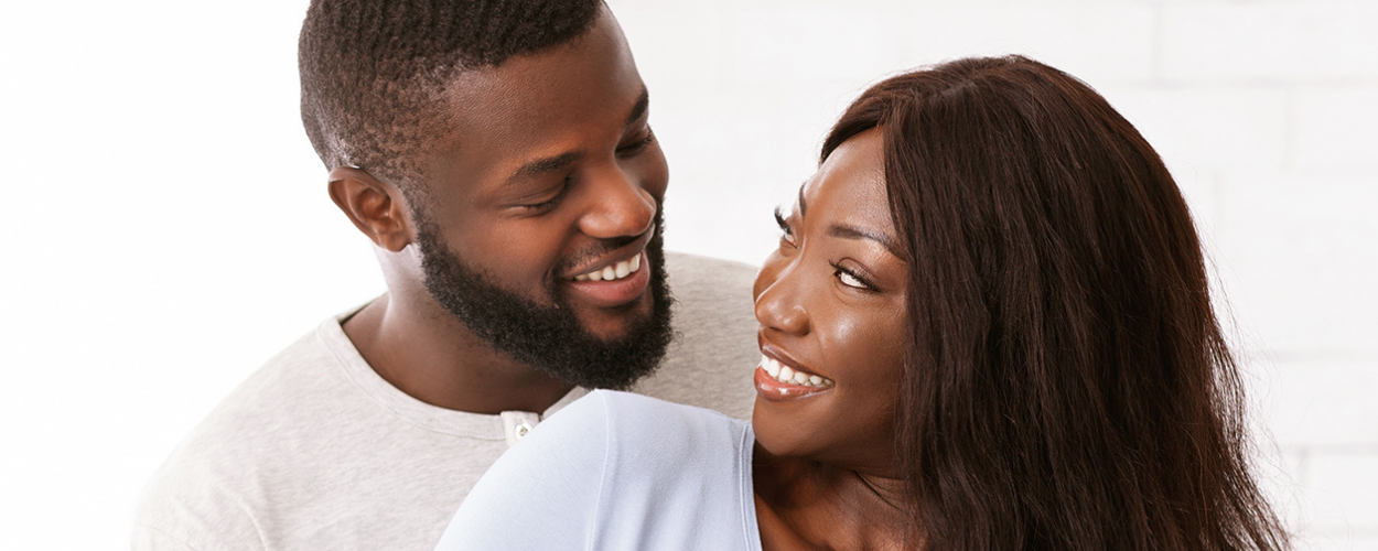 A black man and woman smile at each other while embracing.