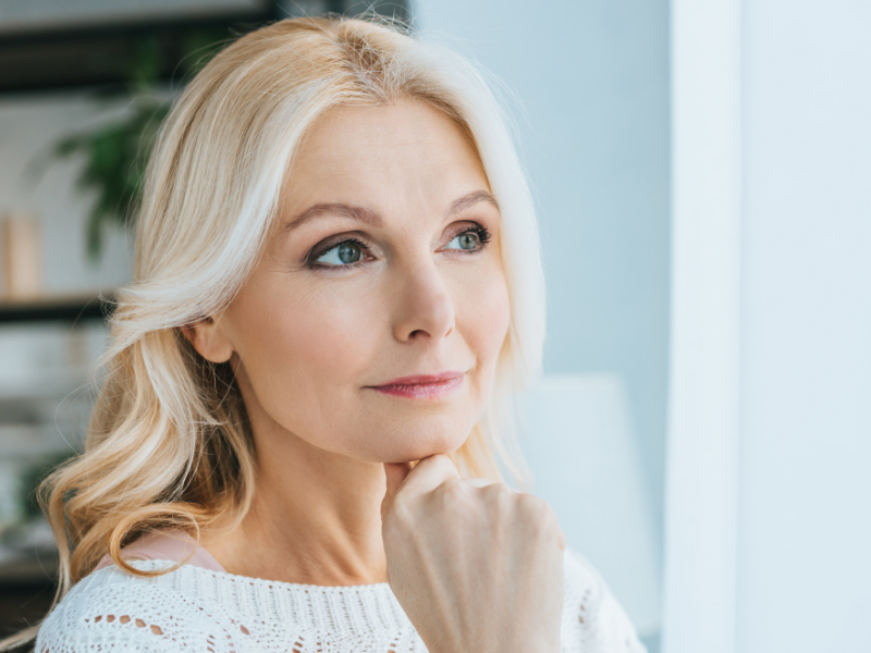 Woman stares out of a window with a pensive expression on her face contemplating Female Sexual Dysfunction symptoms.