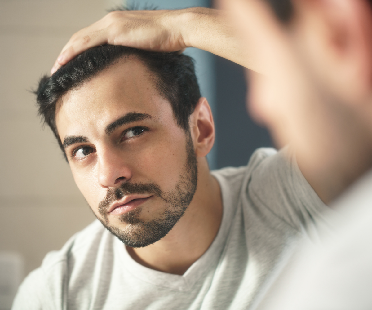 A white man stares pensively in the mirror, studying his hair loss.