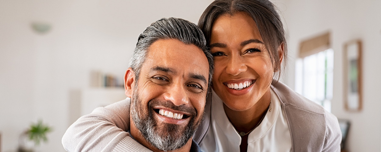 A man and woman smile at the camera as the woman hugs the man from behind, celebrating their treatment of female sexual dysfunction.