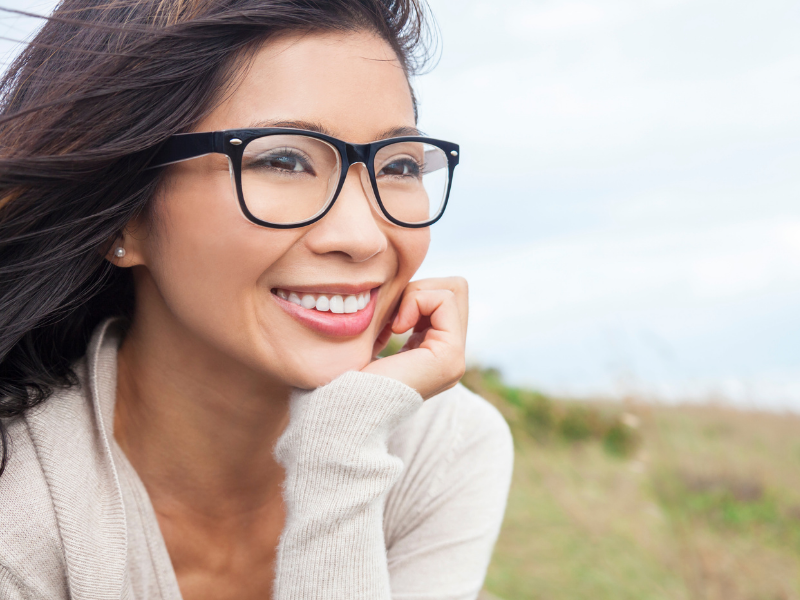 A woman in glasses smiles as she looks to her left.