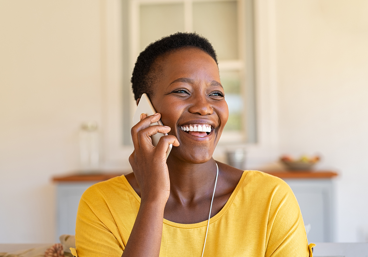 A Black woman laughs happily while talking on the phone.