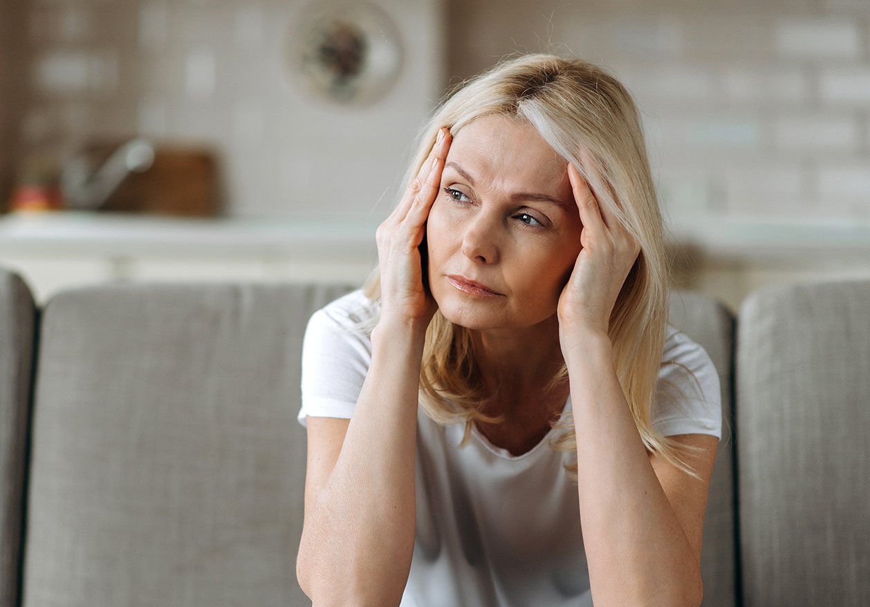 A concerned-looking woman stares to the left while holding her head in her hands as she considers thyroid disease symptoms.