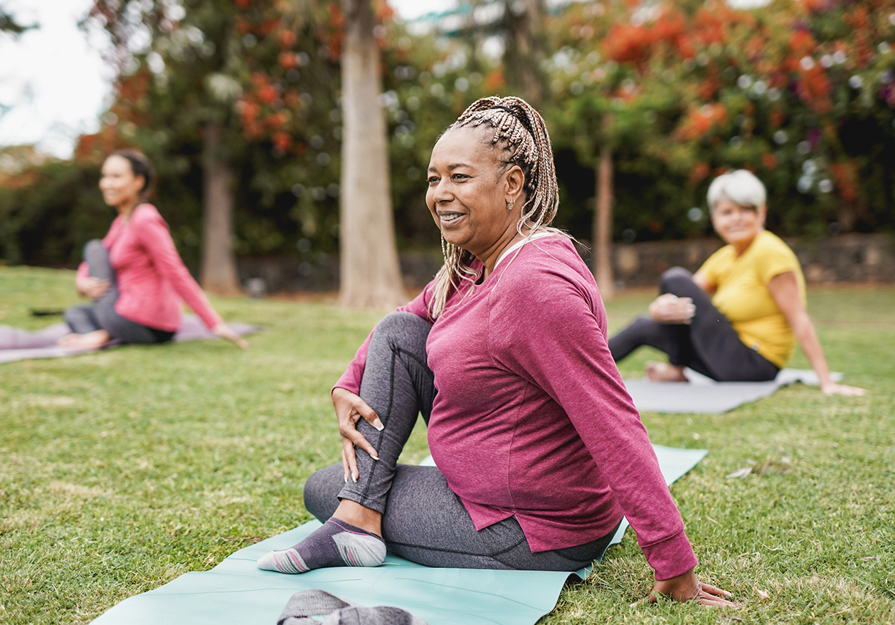 A plus-sized woman stretches on yoga mat on the grass outdoors.