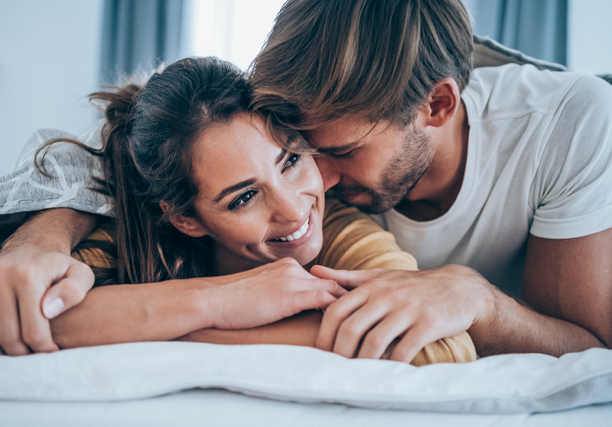A man and a woman in pajamas embrace in bed while smiling to show the benefit of Defy Medical's sexual performance consultations.