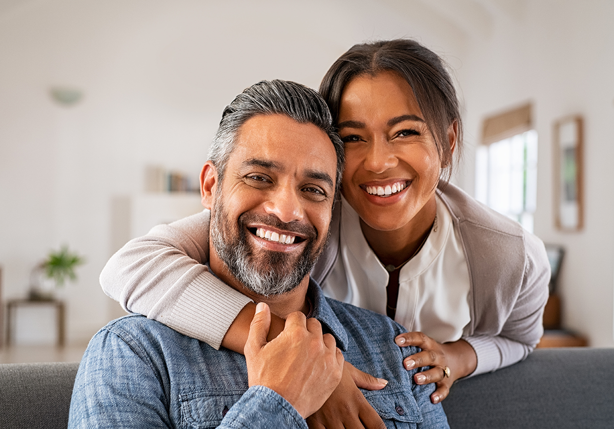 A man and woman smile at the camera as the woman hugs the man from behind, celebrating their treatment of female sexual dysfunction.