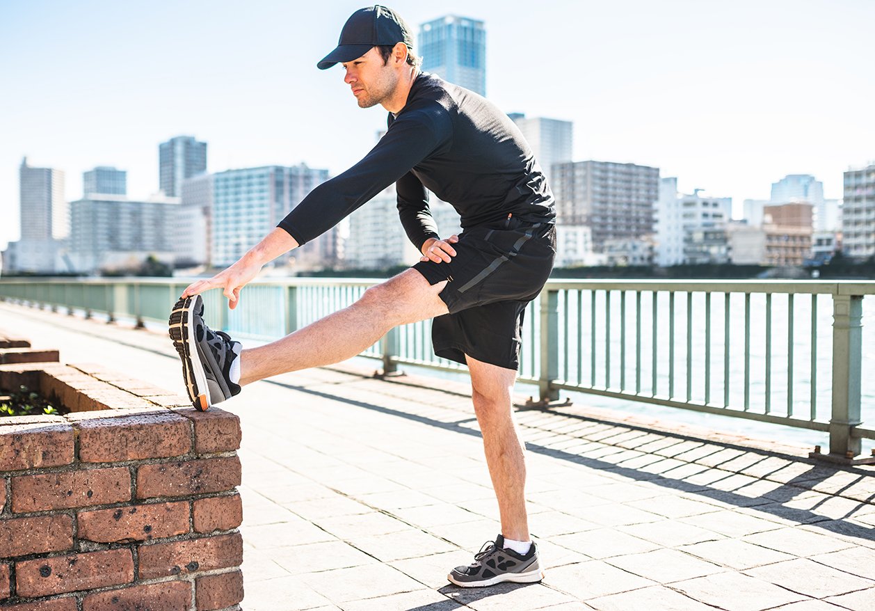 A man in athletic gear stretches his leg during a run on a bridge, showing the potential benefits of anabolic androgenic therapy.