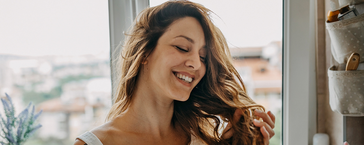 A woman combs her hair while smiling.