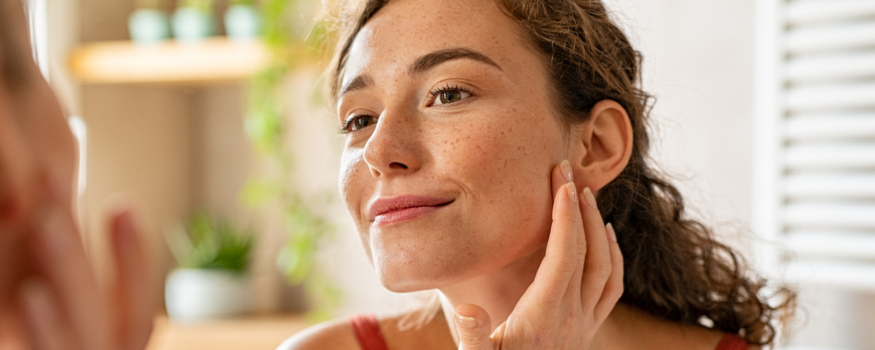 A woman smiles as she looks at her cosmetic injections in the mirror.