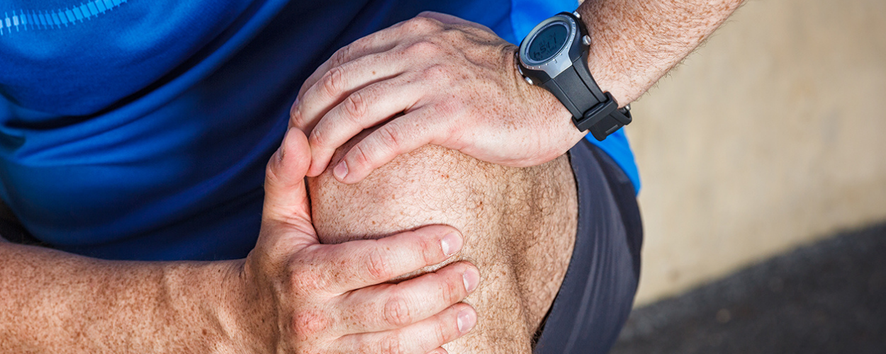 A man in athletic wear massages his knee to indicate joint pain.