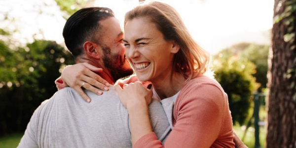A woman hugs a man while both laugh, showing the benefit of ketamine therapy for mental illness.