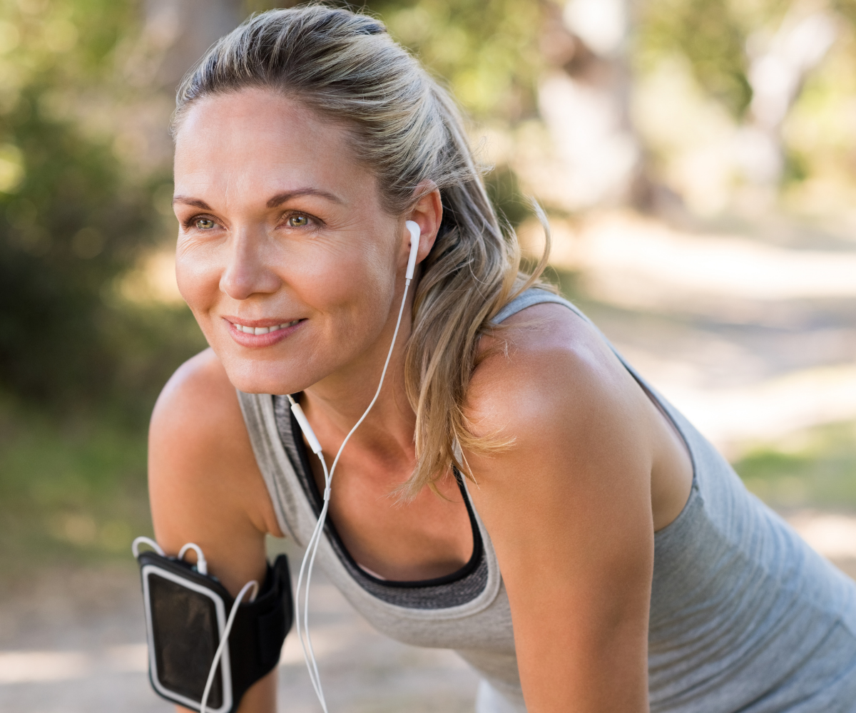 A smiling woman with earbuds pauses on her run.