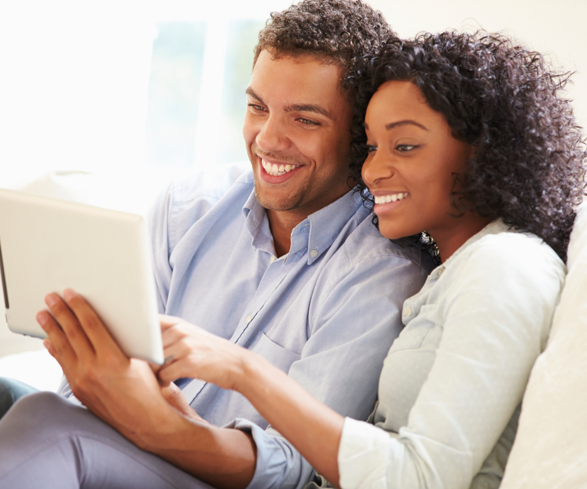 A smiling Black couple stares at a tablet together.