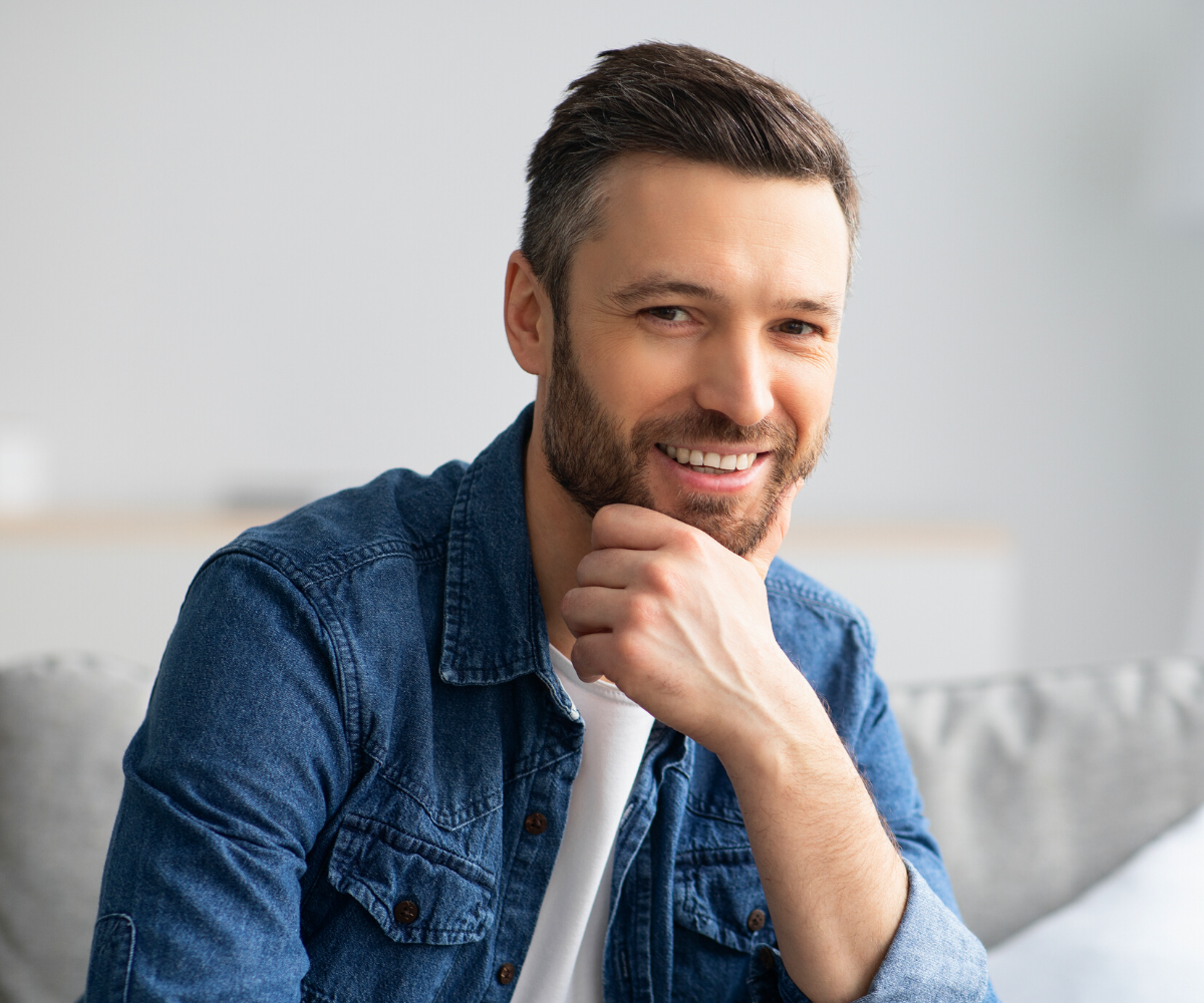 A man smiles with his hand resting on his chin.