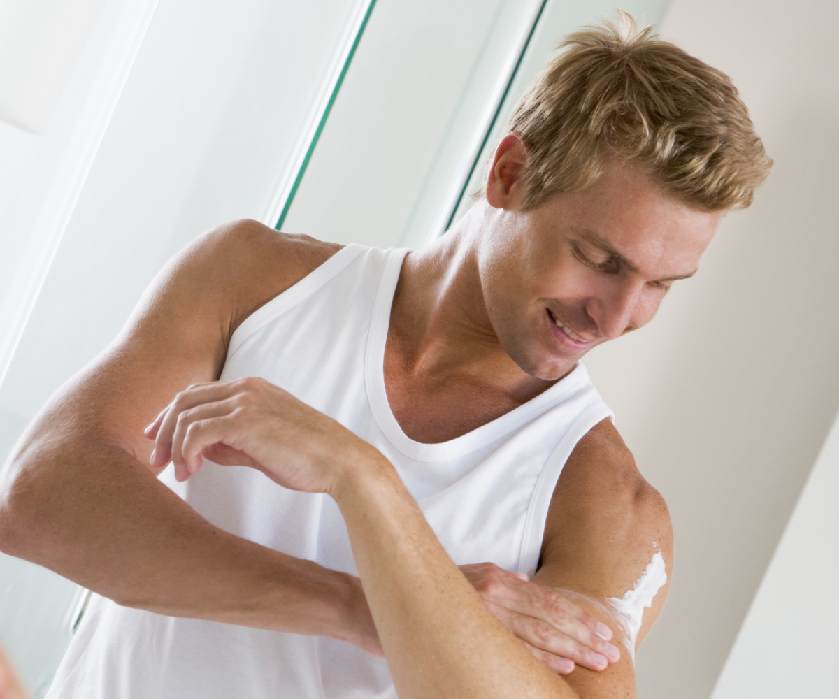 Smiling man applies topical Testosterone to his bare shoulder.