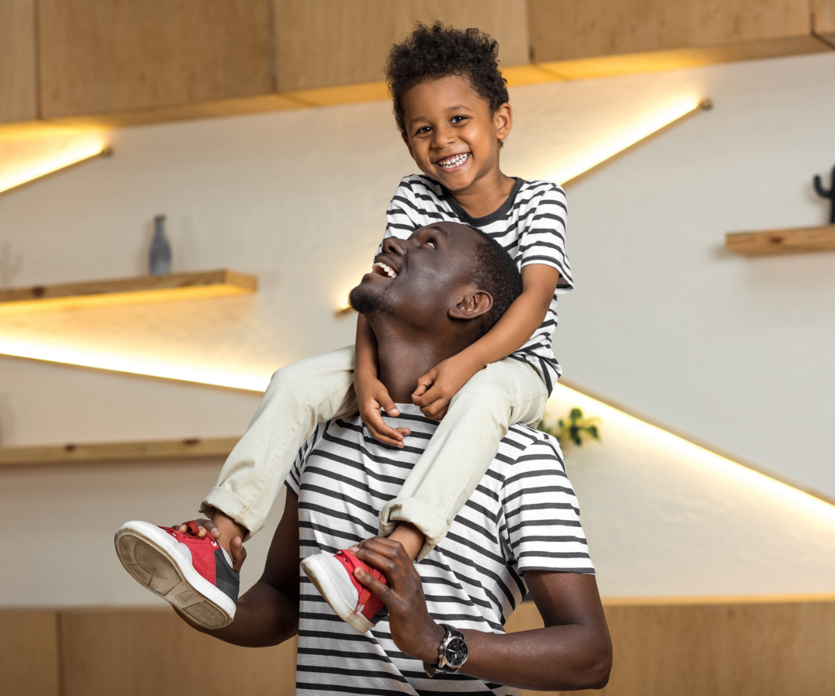 A man carries his son on his shoulders, both smiling.