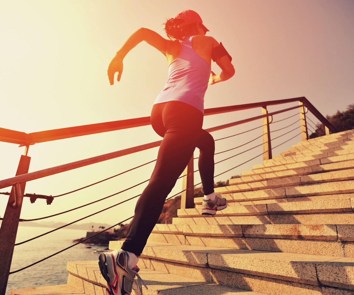 A woman in workout clothes runs up a set of stairs.