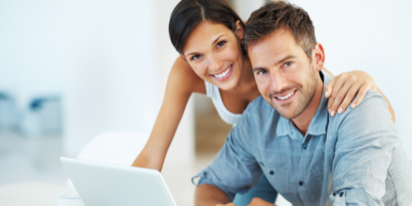 A man and a woman smile while looking at a laptop.