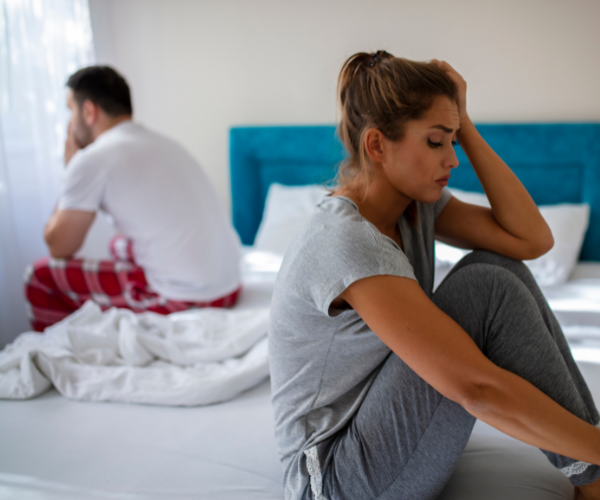 A man and woman facing away from eachother in bed while looking sad and frustrated
