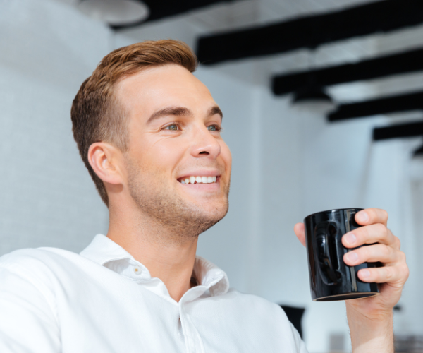 Man with good hair smiling as he holds a coffee cup