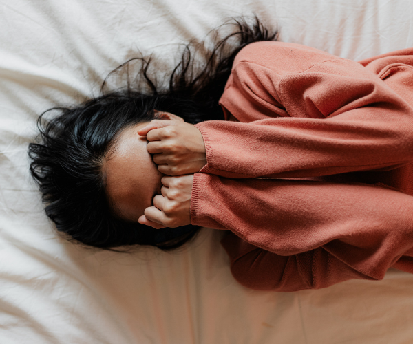 Woman lying in bed with fists clenched over face