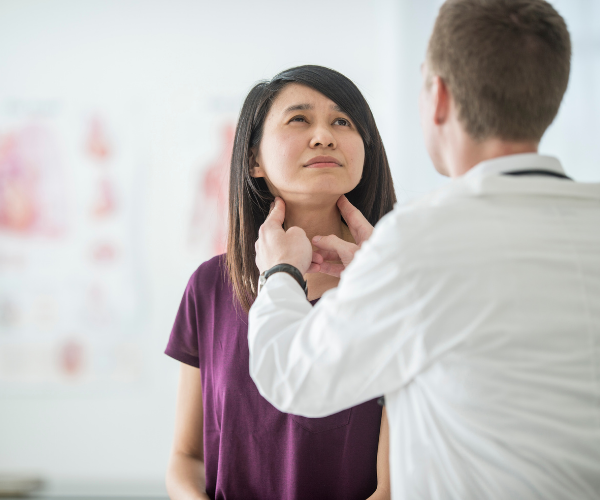 A woman in a doctors office having her thyroid examined.