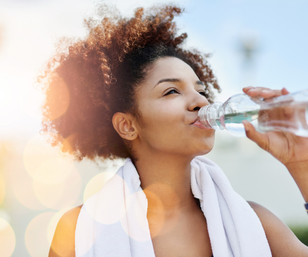 Happy and healthy woman drinking bottle of water with sun shining through background