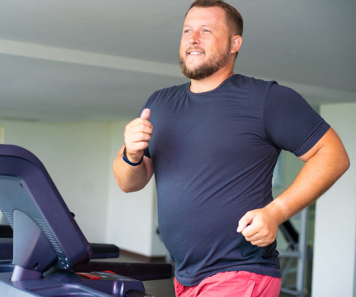 A man runs on a treadmill smiling as he works toward his weight loss program.