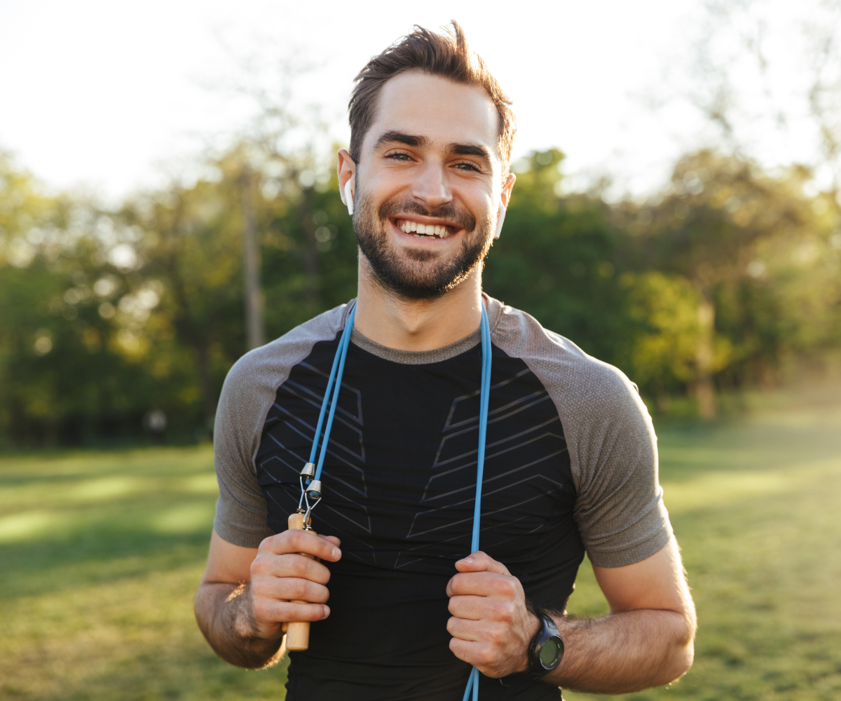 Am active man smiles outdoors with a jump rope draped over his shoulders.
