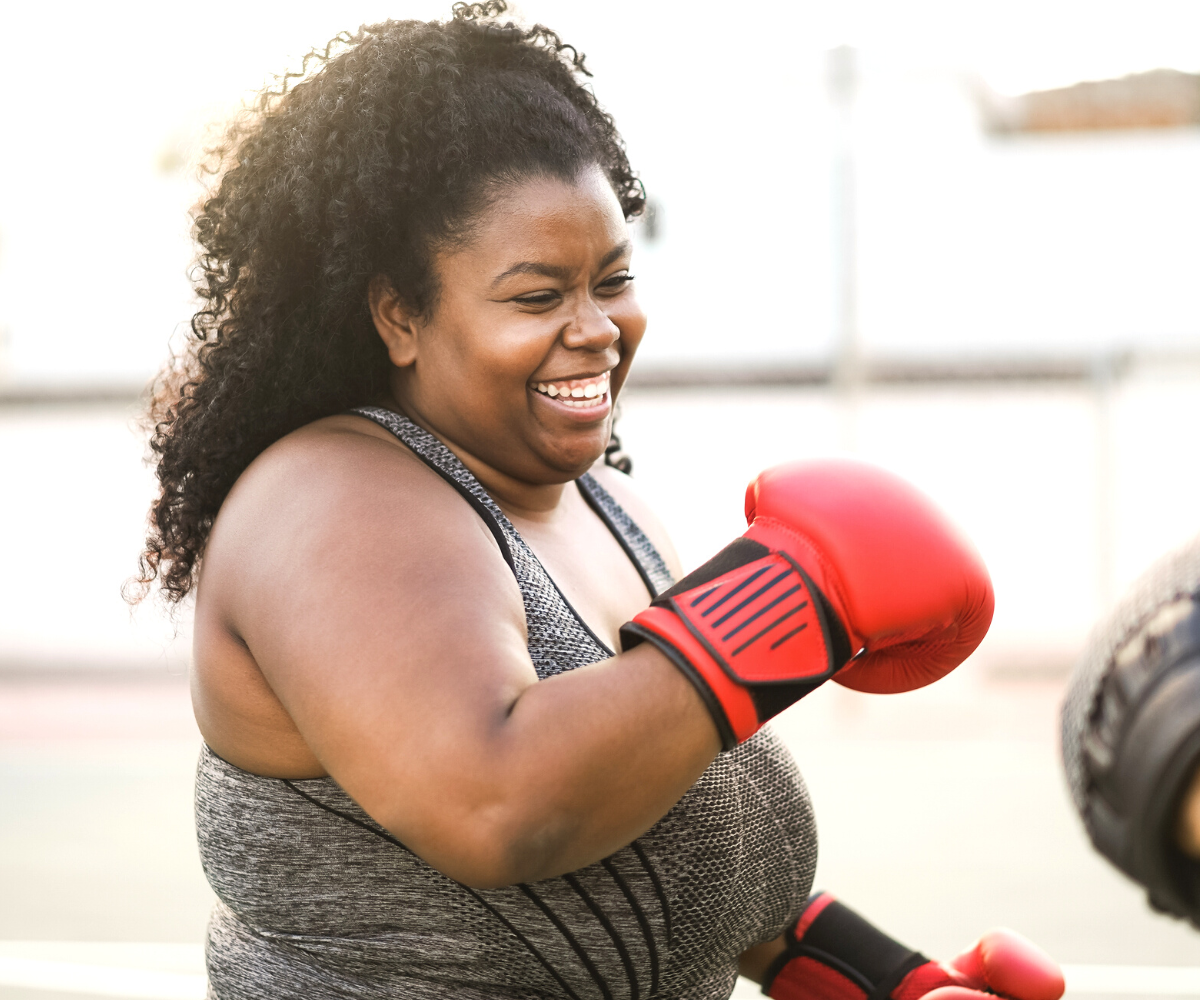 A plus-sized woman smiles as she boxes.