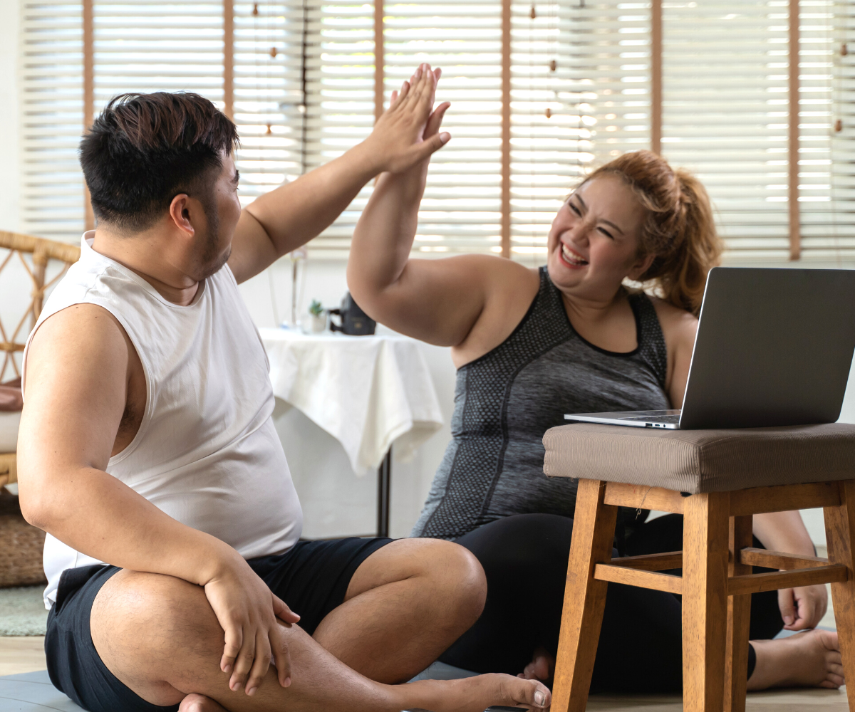 A plus-sized man and woman high five in front of a laptop as they look up GLP-1 agonists for weight loss.
