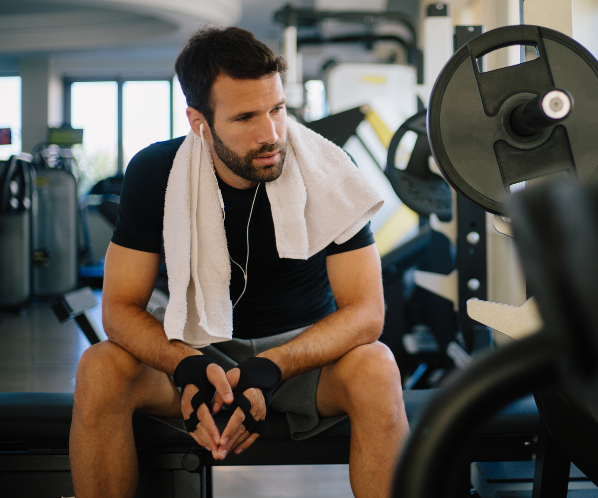 A man sits at the gym to help support his testosterone levels by working out.