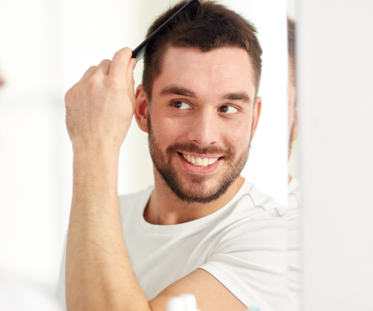 A man smiles as he brushes his hair, because he has strategies to avoid hair loss while on TRT.