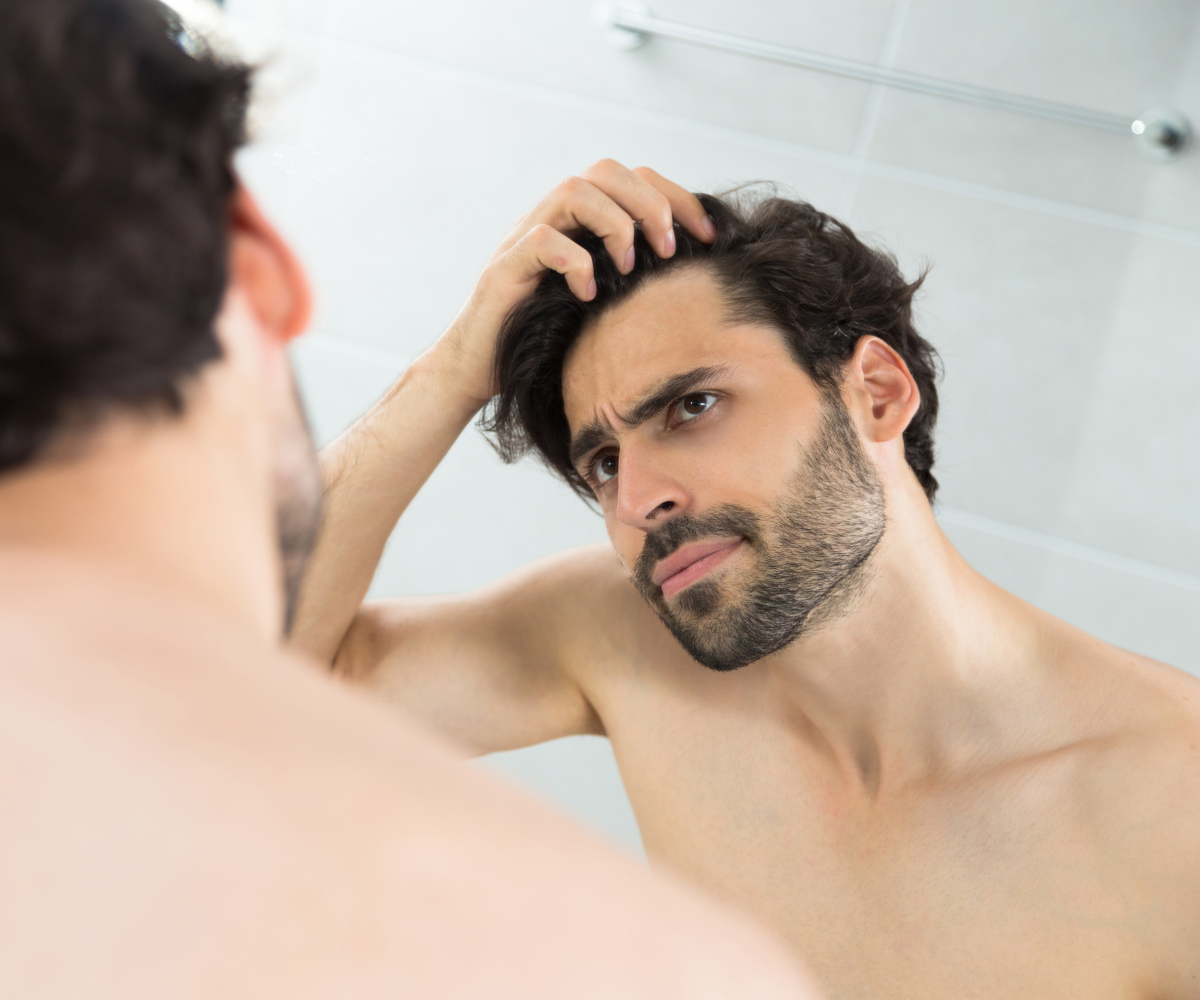 A man examines his hair line as he considers how TRT affects hair loss.
