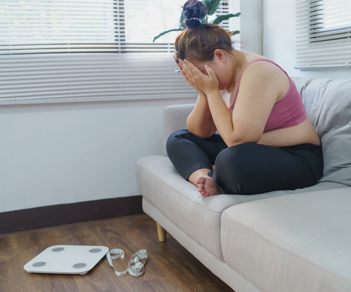 A woman covers her face in her hands after stepping on the scale and realizing she is at a weight loss plateau.