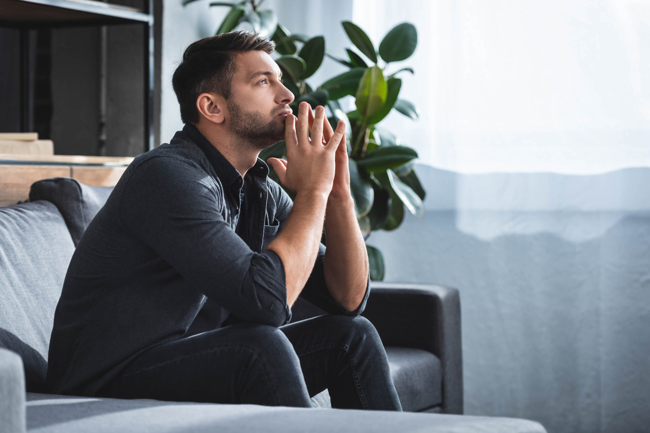 A man sits on the couch with his chin resting on his hands as he contemplates whether masturbation causes low testosterone.